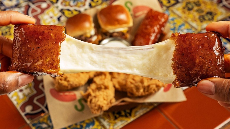 Hands pulling apart Chili's honey chipotle fried mozzarella with Triple Dipper in background
