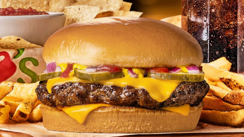 The QP Burger with fries, a drink, chips, and salsa behind it