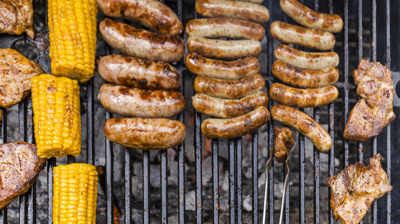 Corn on the cob, sausages, chicken thighs on a grill