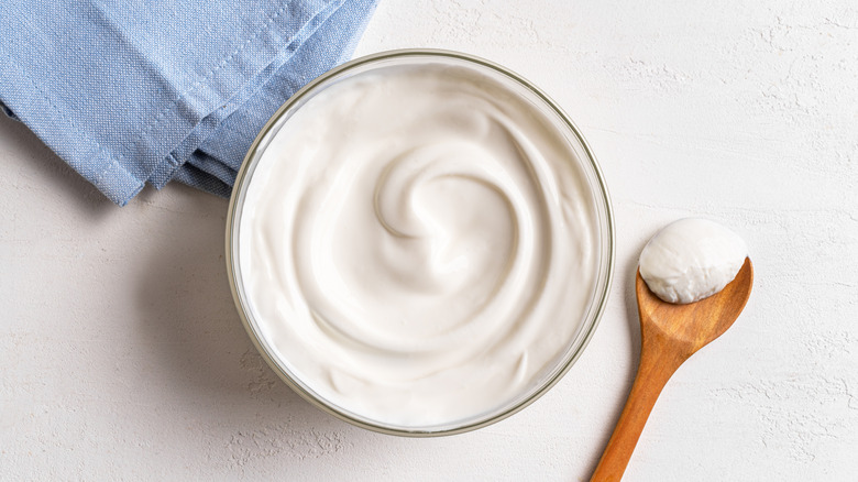 Bowl of sour cream next to wooden spoon and blue napkin