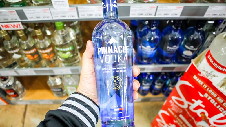A person holding a bottle of Pinnacle Vodka in a store