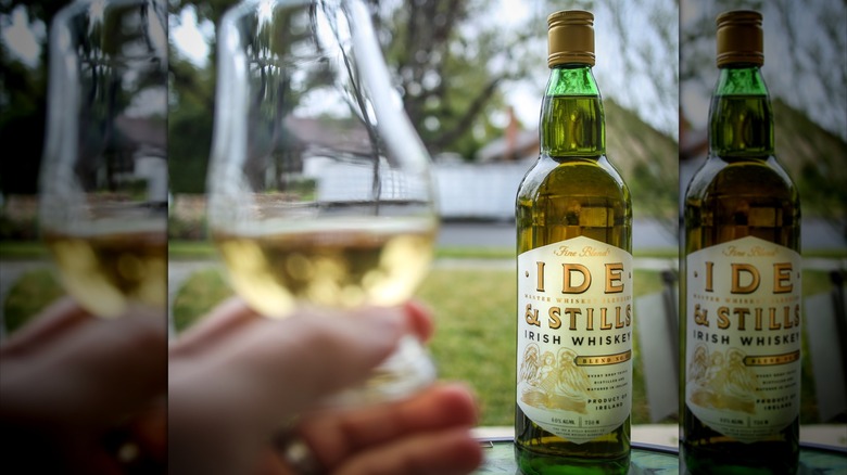 Ide & Stills bottle of whiskey with hand holding a glass blurred foreground