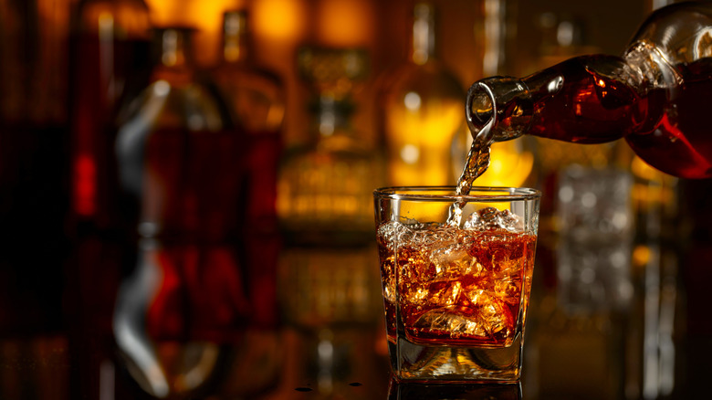 Whiskey being poured into a glass over ice on a dark bar