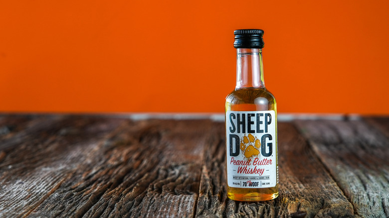 Bottle of Sheep Dog Peanut Butter Whiskey on wooden table with orange background