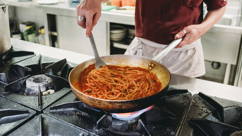 Chef cooking pasta in tomato sauce in a stainless steel pan