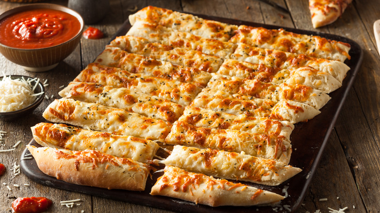 Cheesy bread in tray with marinara sauce on side for dipping.