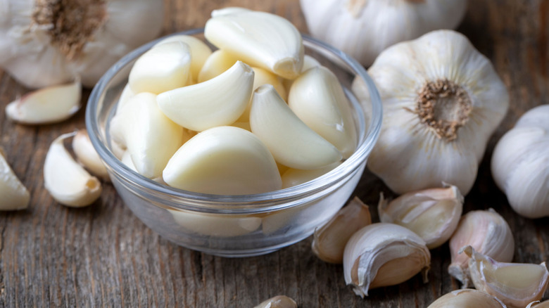 bowl of peeled garlic cloves surrounded by unpeeled heads of garlic