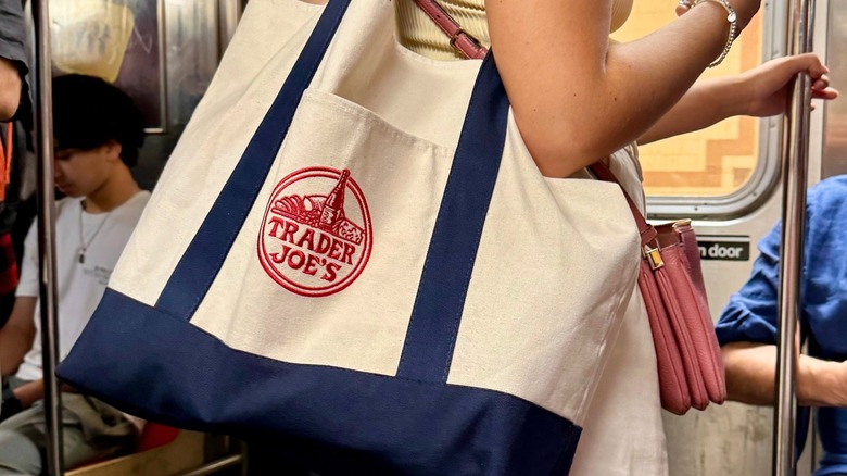 A woman holds a large Trader Joe's tote while riding the subway