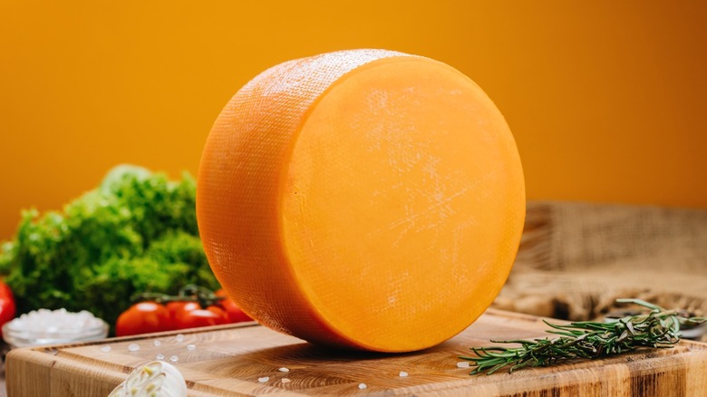A cheese wheel on a wooden cutting board.
