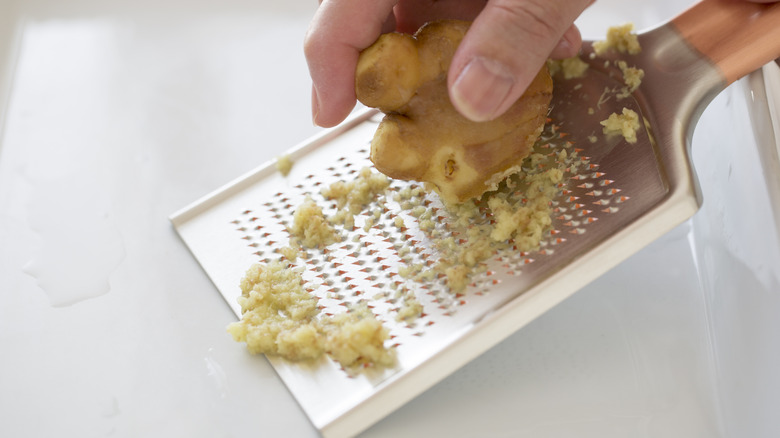 Woman grating ginger over white surface