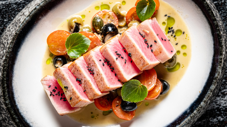 Plate of seared sliced tuna with sesame seeds, assorted vegetables, and creamy broth