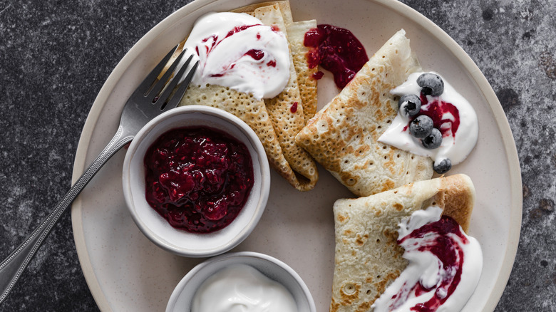 Top down view of crepes with cream, jam, and blueberries