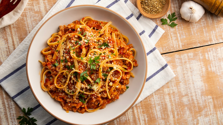 Pasta with a meat based bolognese tomatoes served on white plate with parmesan cheese.