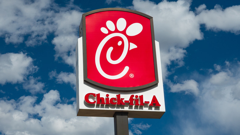 Red and white Chick-fil-A sign showing the chicken logo against a blue sky with fluffy white clouds