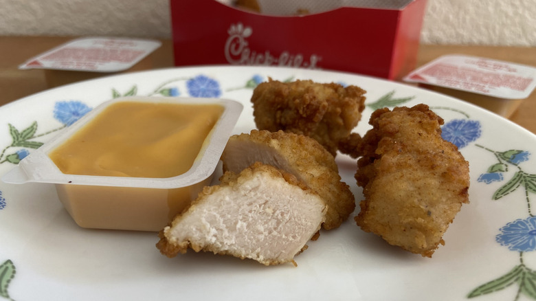 five Chick-fil-A nuggets, one halved, and an open sauce on a small plate, box in background