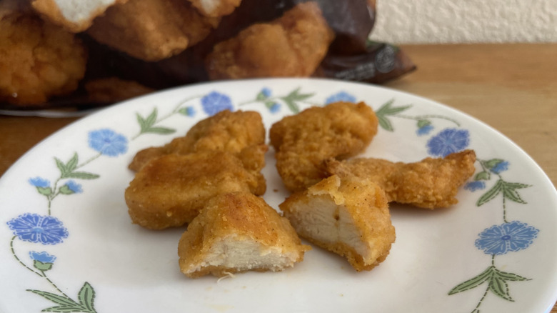 five Costco nuggets on a small plate, one halved, bag in background