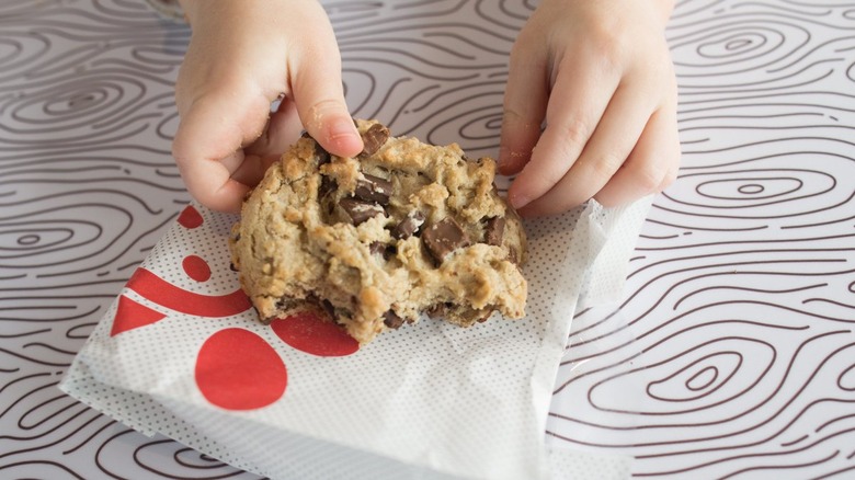 Hands holding partially eaten chocolate chip cookie on a Chick-fil-A wrapper
