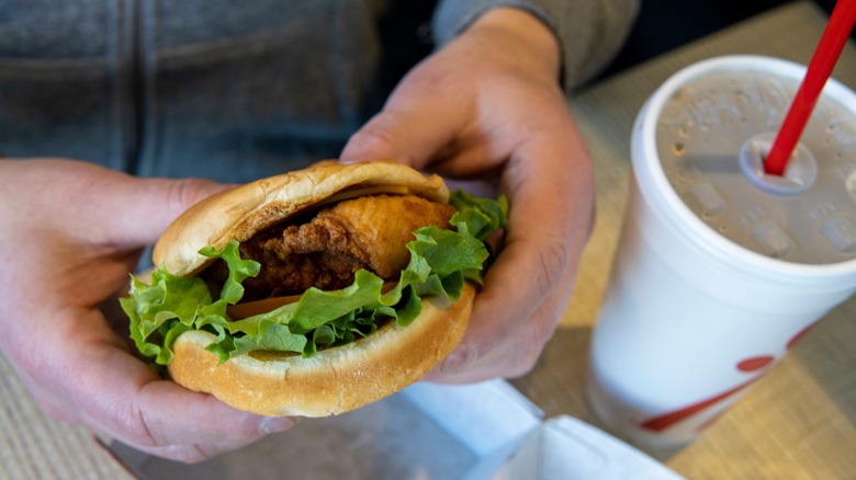 Hands holding Chick-fil-A chicken sandwich next to drink