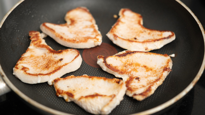 five chicken breasts searing in a frying pan