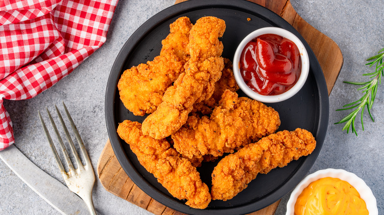 A plate of golden chicken tenders with dipping sauces on the side