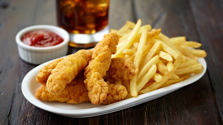 A plate of chicken tenders and fries with ketchup and soda on the side