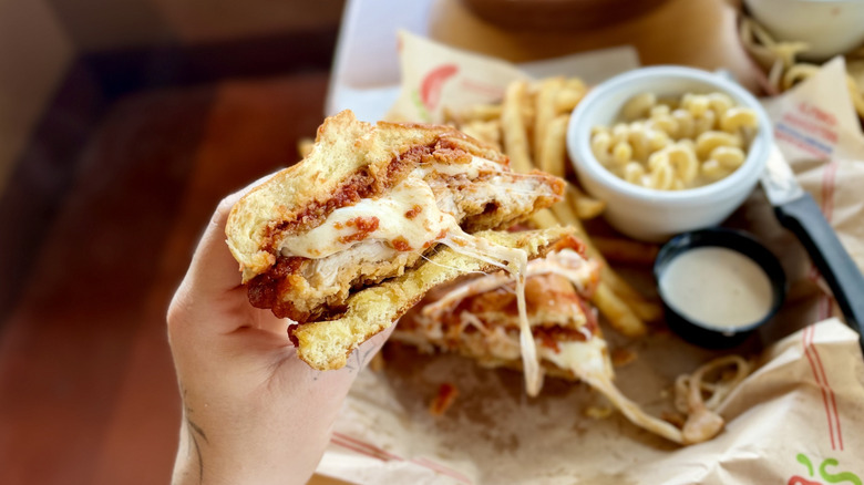 Hand holding a Chili's Chicken Parm Big Crispy sandwich with a bite taken