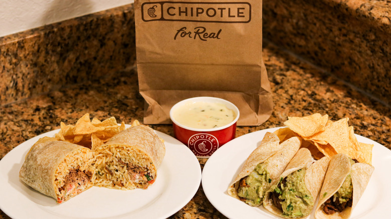 Chipotle burrito and chips on plate next to three tacos on plate