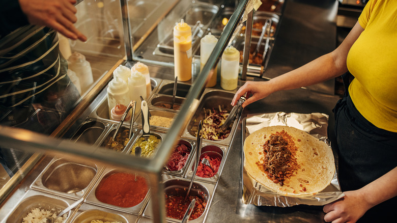 A fast food worker preparing a burrito for a customer.