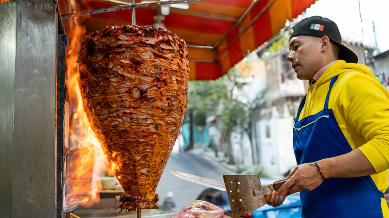 man preparing to cut pork from rotating spit