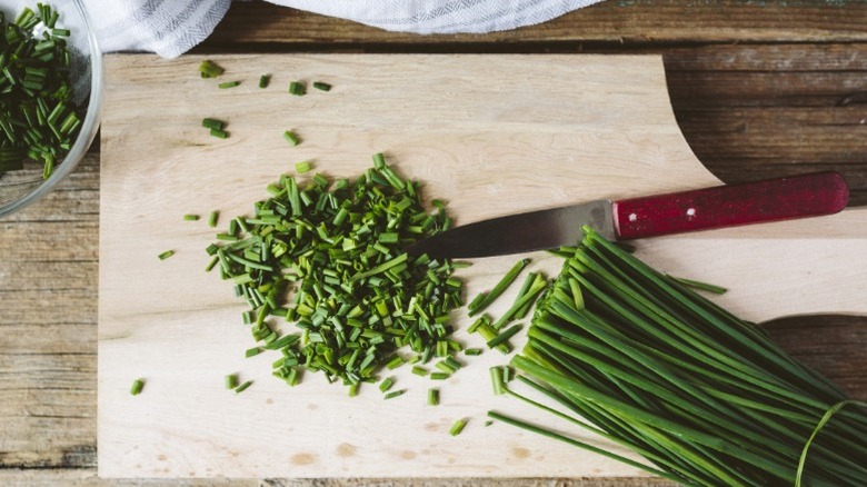 Chives chopped up on a wooden cutting board.