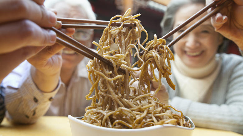 People using chopsticks to share in a bowl of noodles