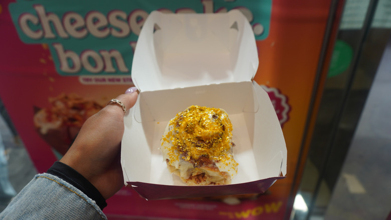 A hand holding a Cinnabon Butterbeer-flavored Classic Roll in its box