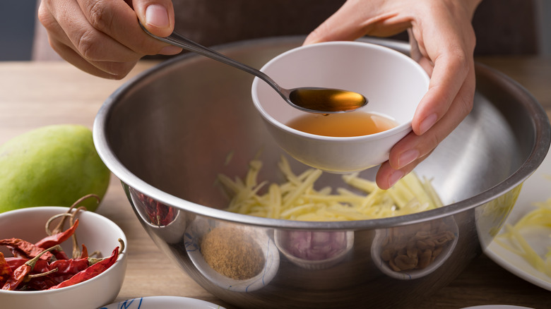 Hand spooning fish sauce into metal bowl with green papaya