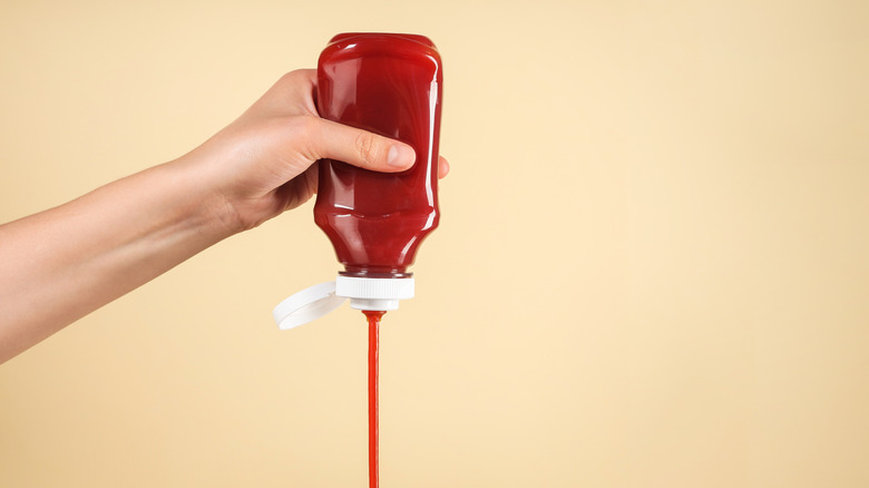 Hand squeezing a stream of ketchup from a bottle