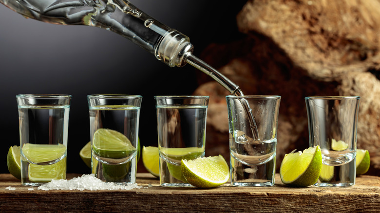 Pouring tequila into shot glasses next to lime wedges