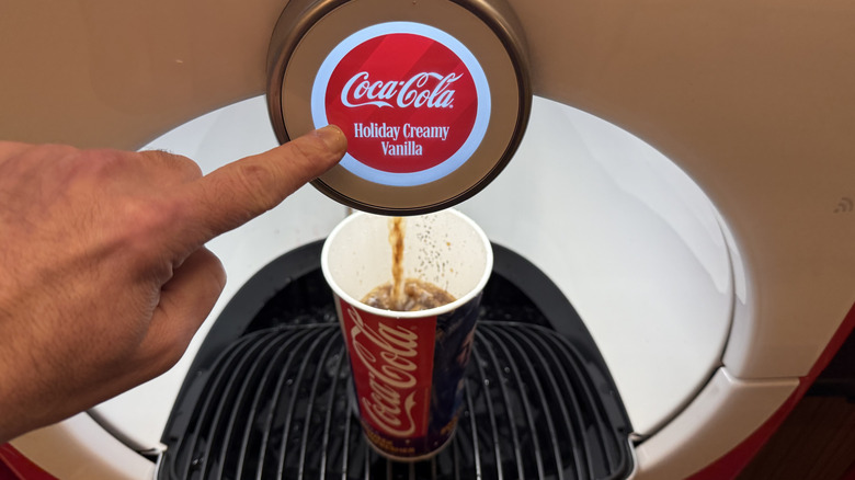 Hand pressing button to pour Coca-Cola Holiday Creamy Vanilla into a cup