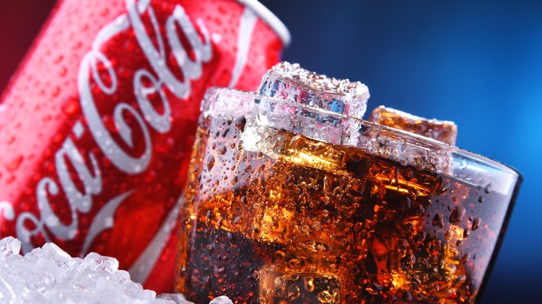 A glass of Coca-Cola, with a can in the background.