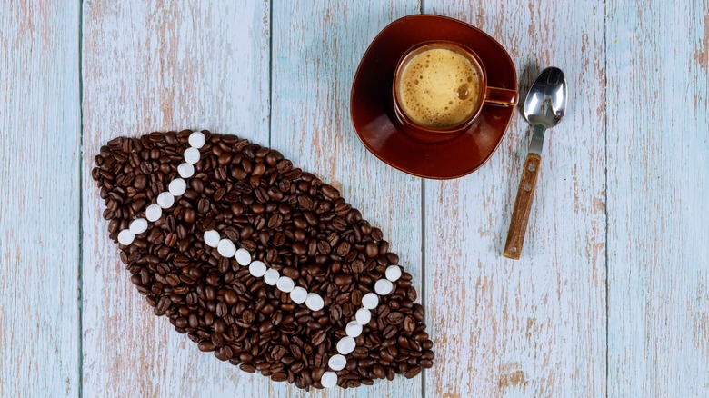 A tabletop with a cup of coffee, teaspoon, and coffee beans arranged in the shape of an American football