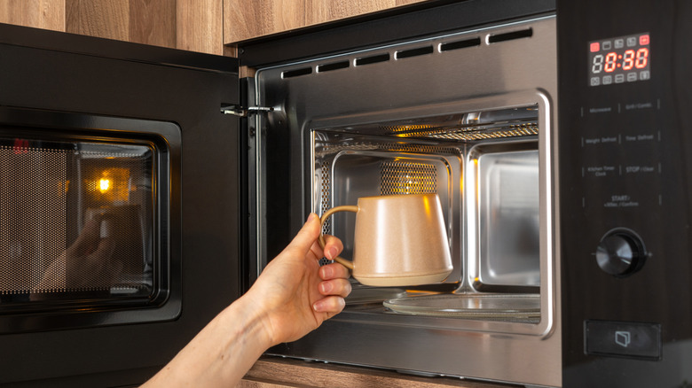 Hand putting coffee mug in microwave