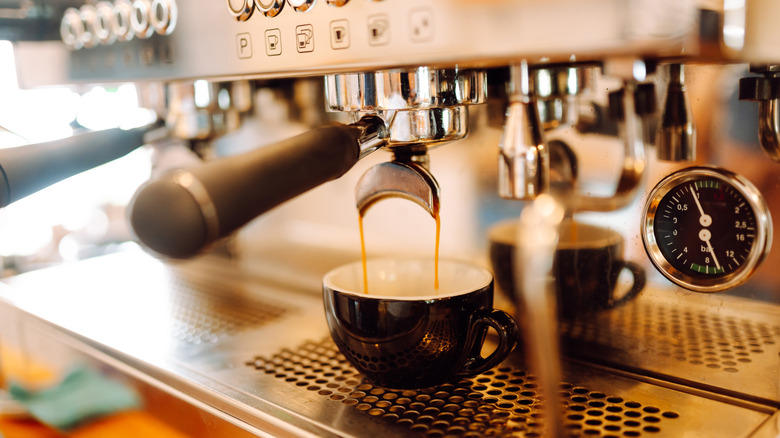 An espresso machine pouring espresso into a black and white cup.
