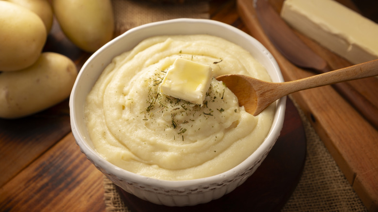 A bowl of mashed potatoes with a pad of butter on top and a wooden spoon