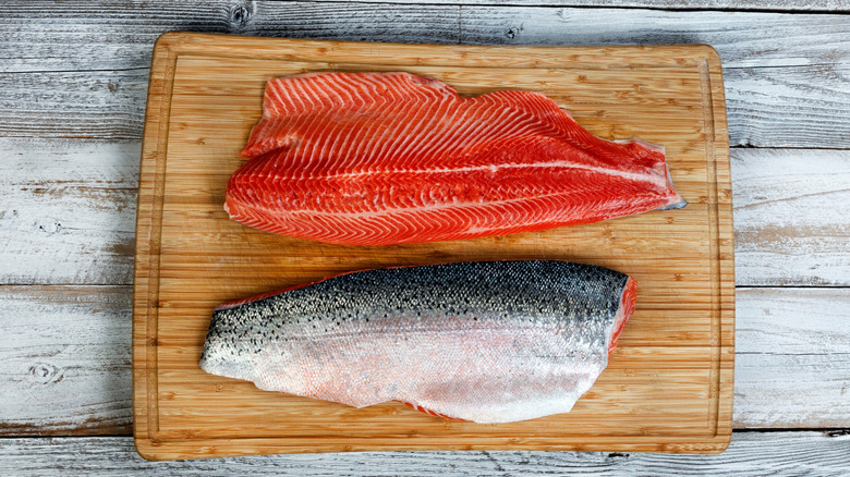 Two salmon filets skin side up and skin side down on wooden cutting board