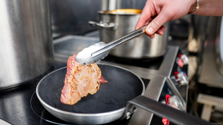 Person flipping fish filet on pan on stovetop with metal tongs
