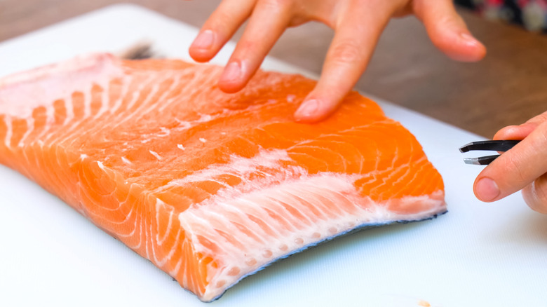 Person removing bones with fish tweezers from salmon filet