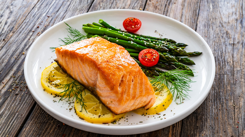 Cooked salmon filet on a white plate with asparagus, tomato, and lemon