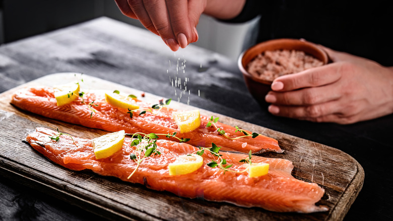 Person seasoning two salmon filets with salt on wooden cutting board