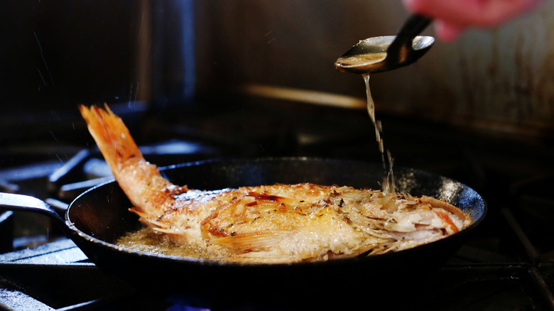 Whole fish on a cast iron frying pan in boiling liquids