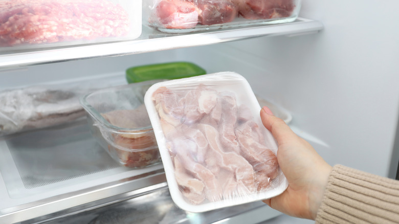 A person holding frozen meat in a freezer