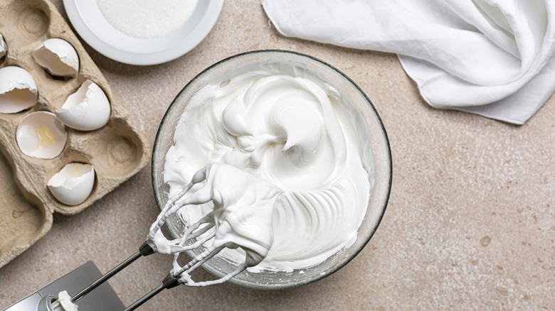 Beaten egg whites with sugar for meringue in a mixing bowl with an electric hand whisk