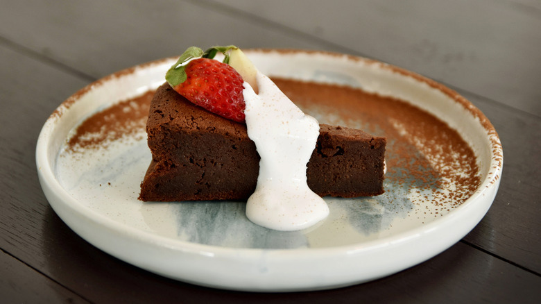 A rich, flourless chocolate cake topped with whipped cream and fresh strawberry, served on a ceramic plate